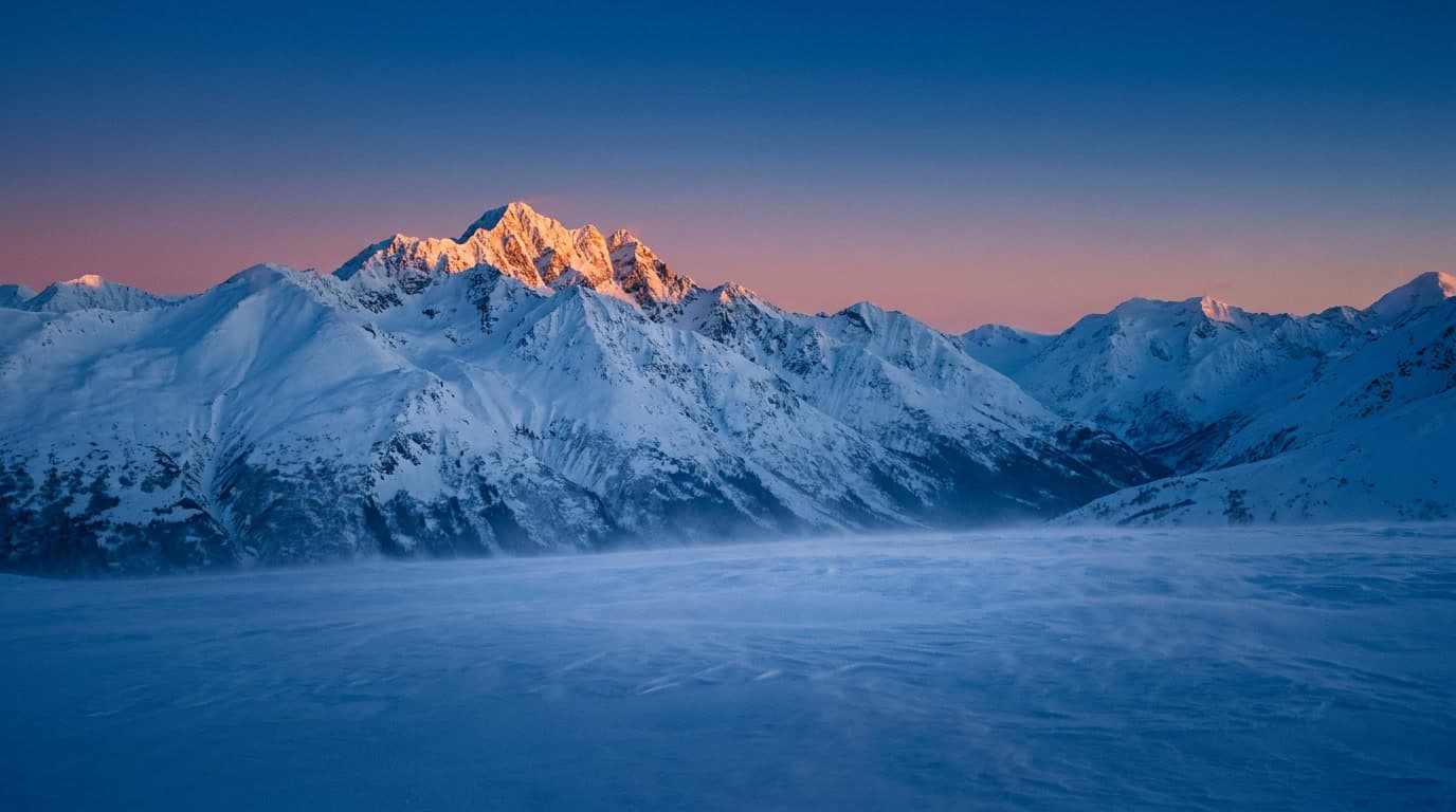 The Chugach Mountains east of Anchorage at deep blue hour, the highest peaks catching the first warm alpenglow above an undisturbed snow foreground.